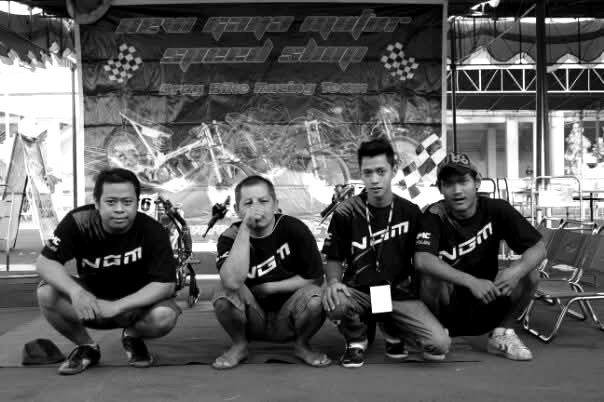 Four NGM team members crouched in front of the racing banner