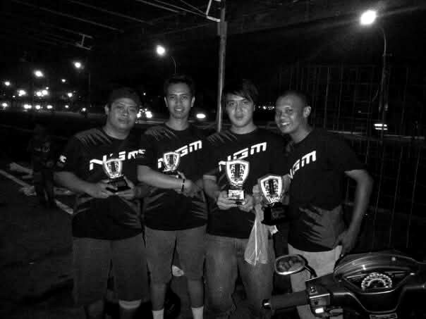 Four NGM team members holding racing trophies at night
